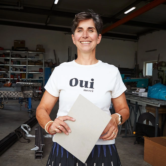 Eine Frau steht in einer Werkstatt mit einem Zettel in der Hand. 