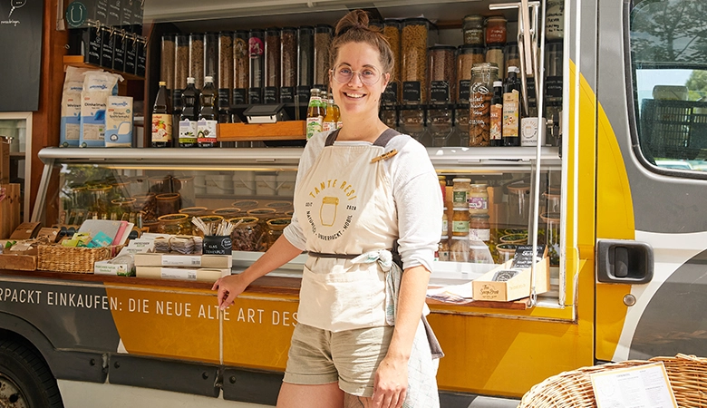 Eine Frau steht vor einem Verkaufswagen mit unverpackten Lebensmitteln.